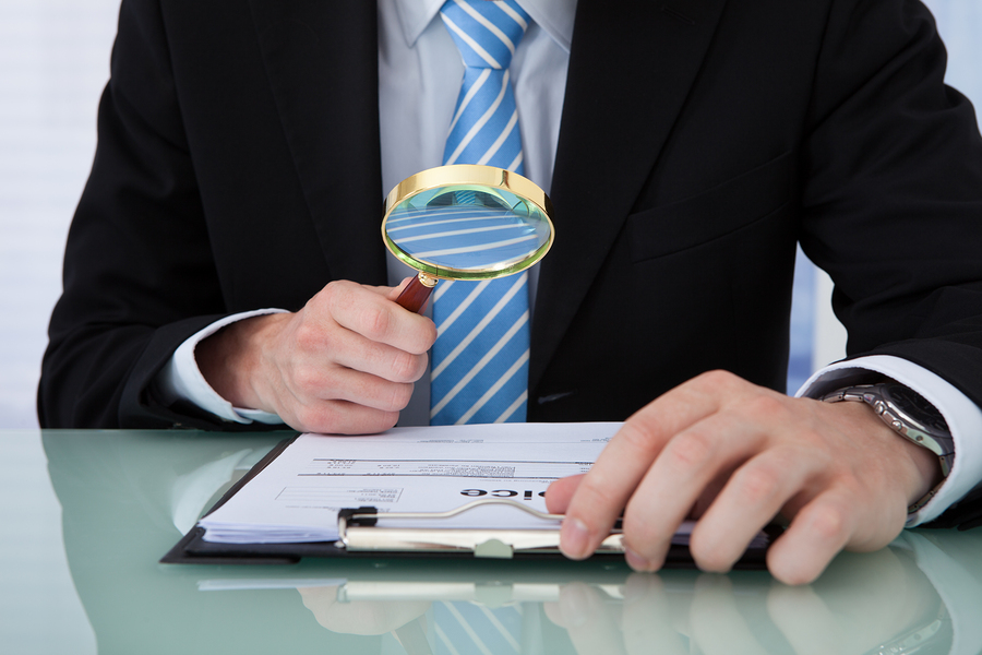 businessman examining invoice through magnifying glass