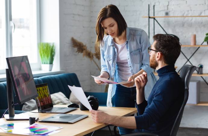 Graphic designer and his colleague discussing about photos while he is working with his laptop, monitor and drawing tablet.