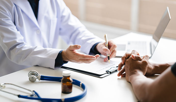 Doctor in lab coat discussing medical paperwork with patient with stethoscope on desk