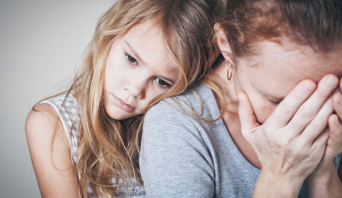 Grieving mother with hands over face comforted by her young daughter