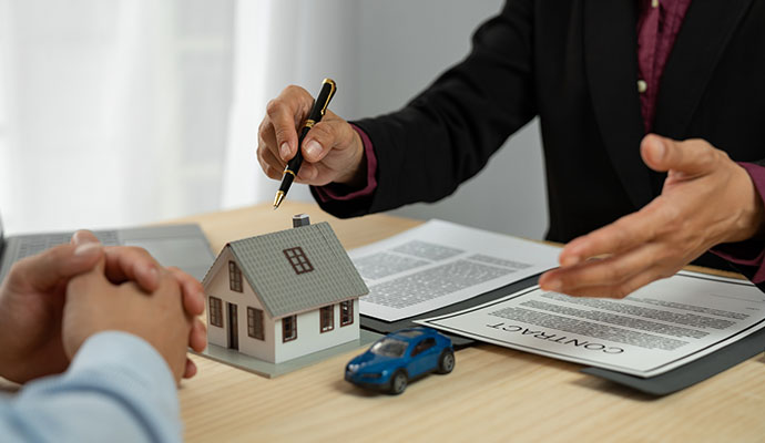 Insurance advisor pointing to house model and toy car with client policy documents