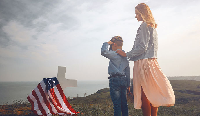 Mother and young son saluting memorial cross draped with American flag